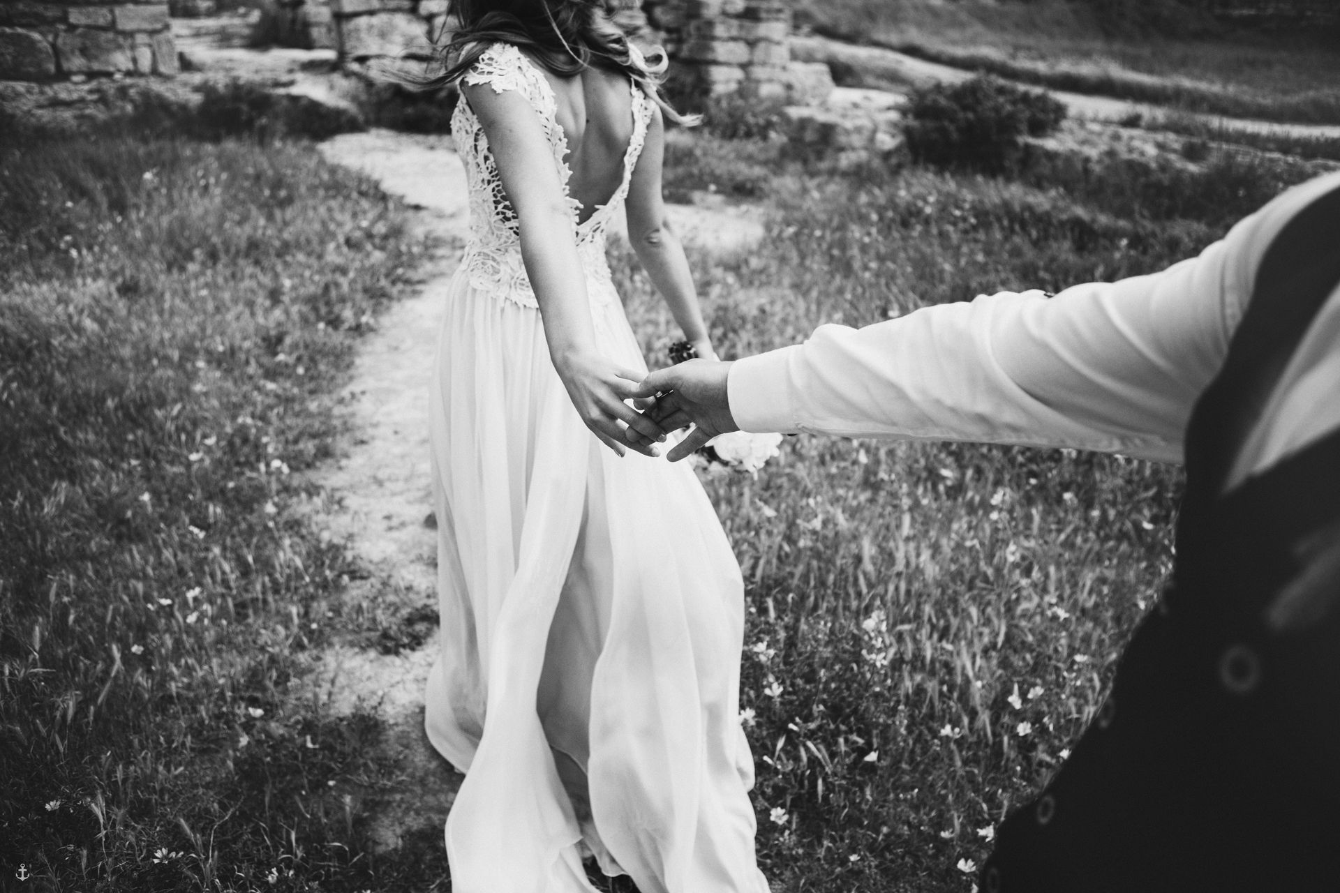 Un couple se tenant la main, marchant dans l'herbe. La femme porte une robe de mariée blanche