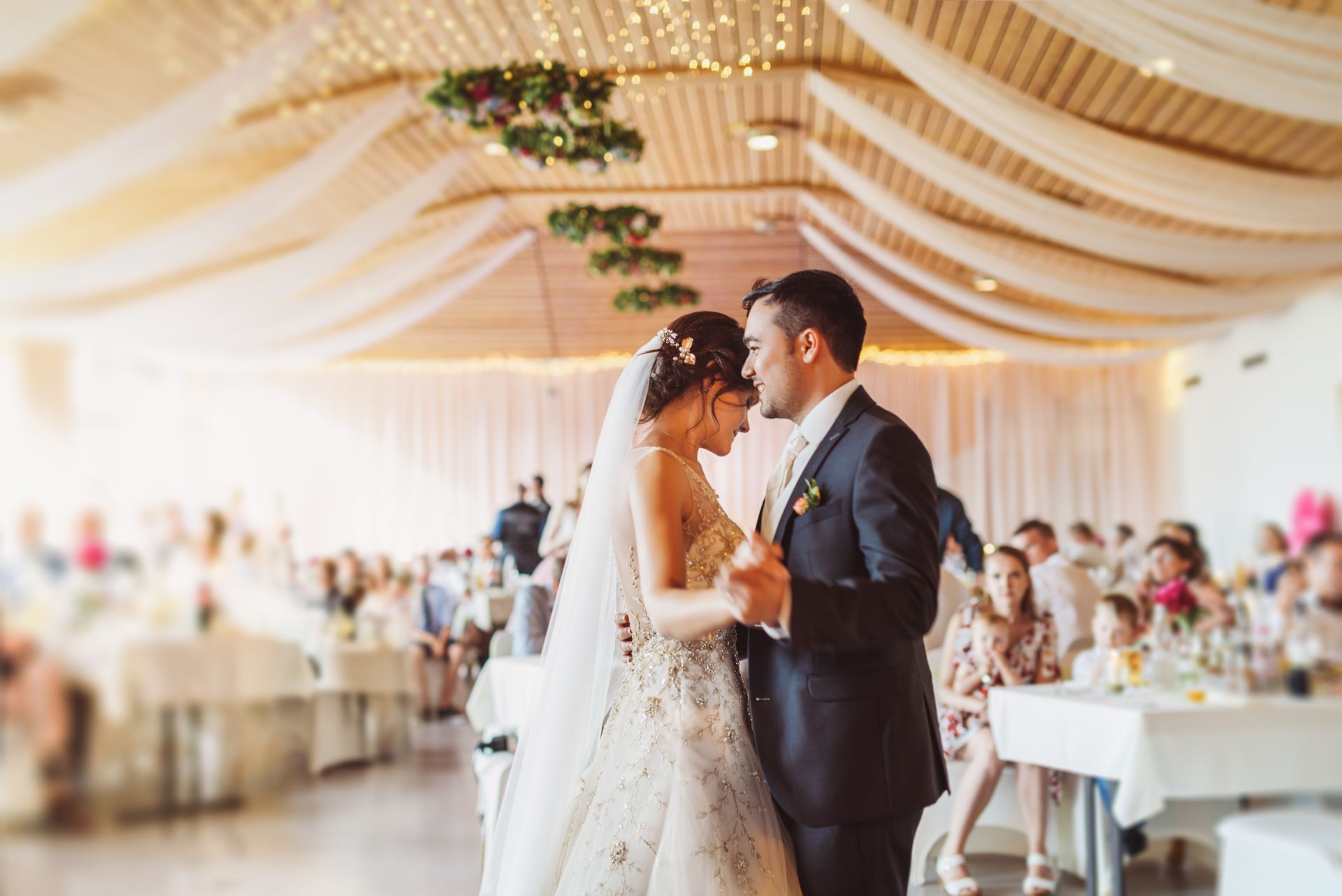 Un couple danse à leur réception de mariage, plafond décoré de draperies et de lumières, invités attablés
