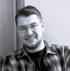 Ein Schwarzweißfoto eines Mannes mit Brille und kariertem Hemd.