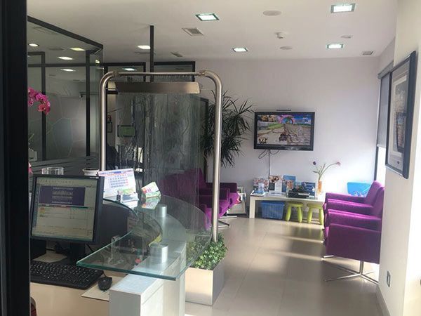 Una sala de espera con sillas moradas y un televisor en la pared.