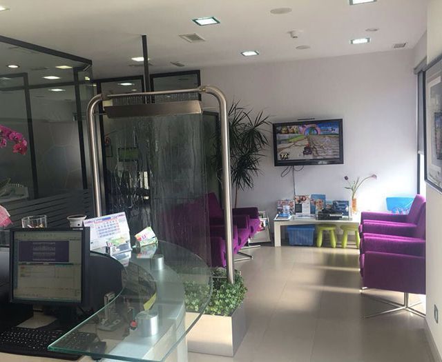 Una sala de espera con sillas moradas y un televisor en la pared.