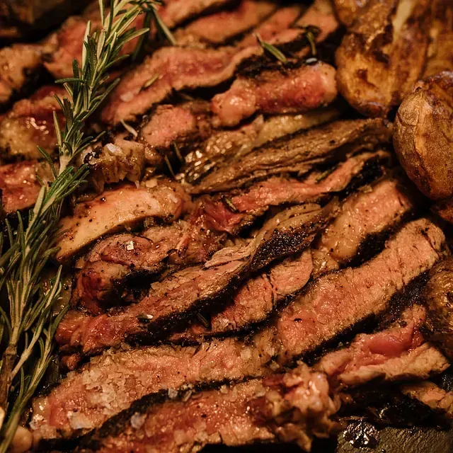 Filete de ternera a la parrilla en rodajas con ramita de romero y patatas asadas.