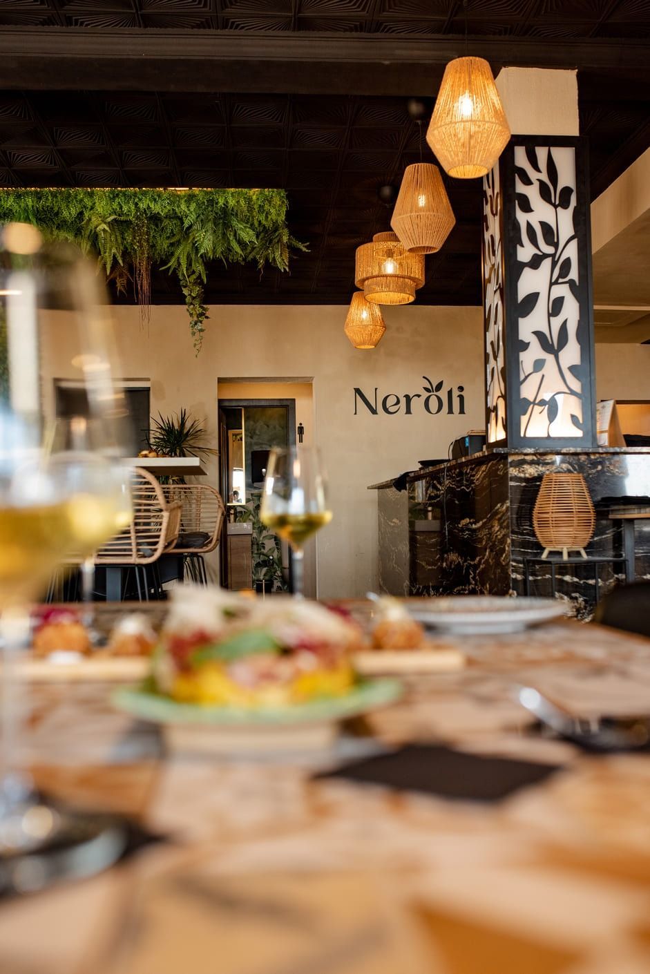 Interior del restaurante con lámparas de mimbre, vegetación, comida y la palabra 