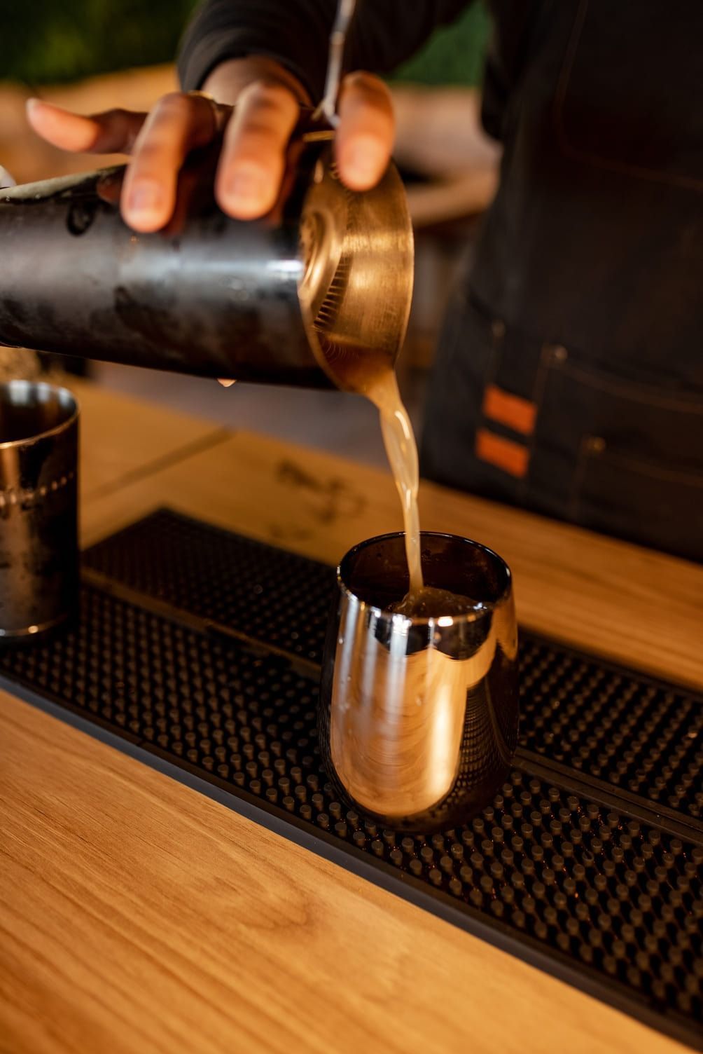 Un camarero sirve una bebida de una coctelera a una jarra de plata en la barra.