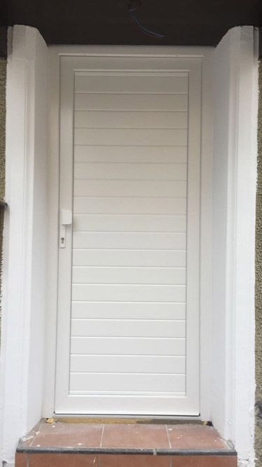Una puerta blanca está encima de un porche de ladrillo.