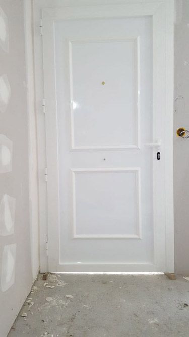 Una puerta blanca está en una habitación al lado de una pared.