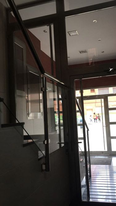 Una escalera en un edificio con barandilla de vidrio y una puerta.