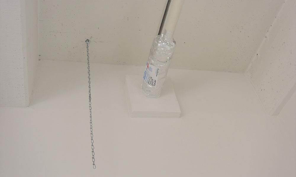 Ein weißes Rohr liegt neben einer Kette auf einer weißen Fläche.