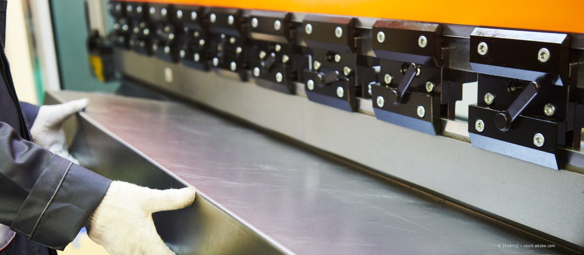 Ein Arbeiter mit Handschuhen handhabt ein Metallblech an einer Industriemaschinenlinie.