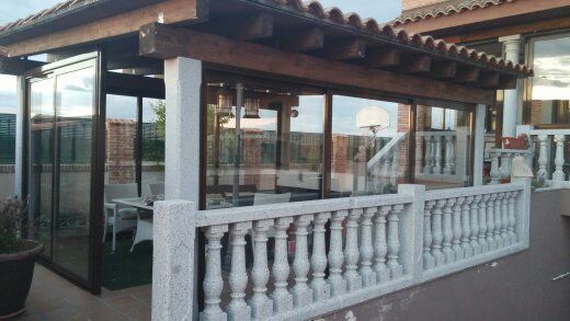 Patio cerrado con paredes de vidrio, techo de madera y balaustrada blanca con vista a un patio.