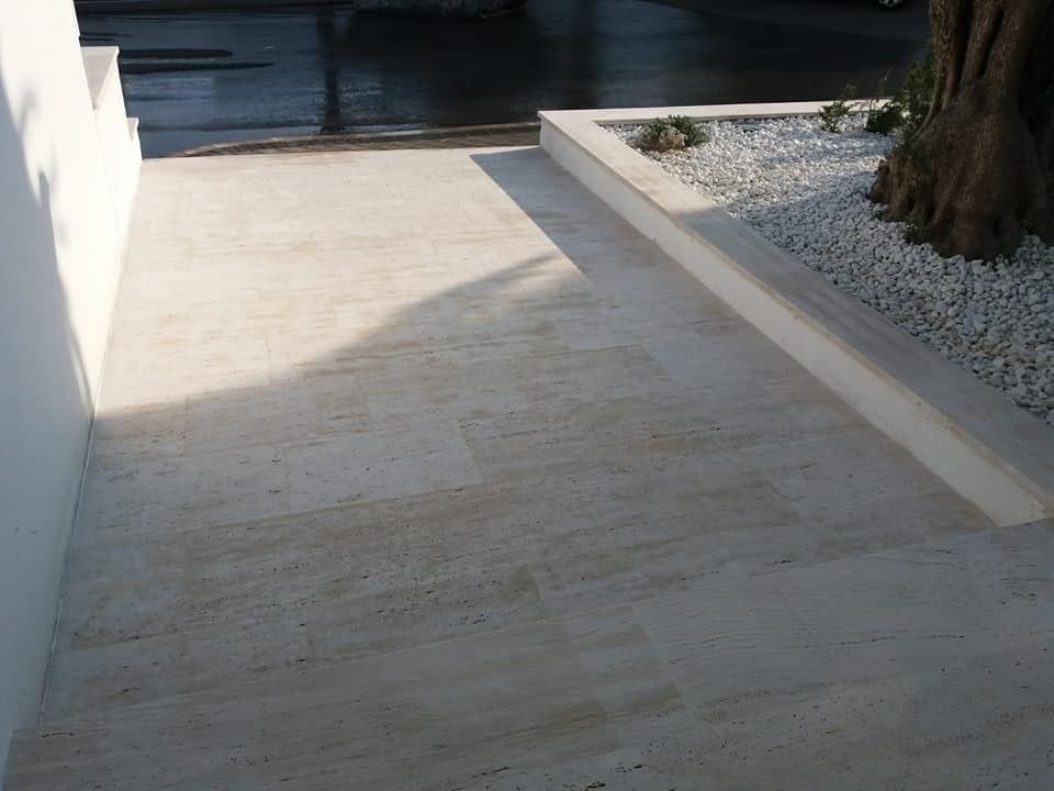 Patio de piedra clara con jardinera llena de guijarros blancos. Muro a la izquierda, escaleras y calle al fondo.