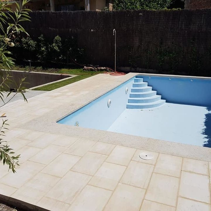 Piscina azul vacía con marco de azulejos de color claro y escalones; entorno al aire libre.