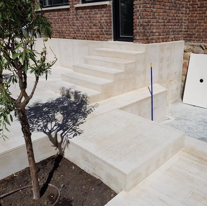 Escaleras de hormigón que conducen a un edificio de ladrillo. Un pequeño árbol proyecta sombra en el rellano inferior.