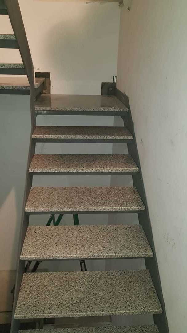 Escalera de metal con peldaños de granito sobre paredes blancas.
