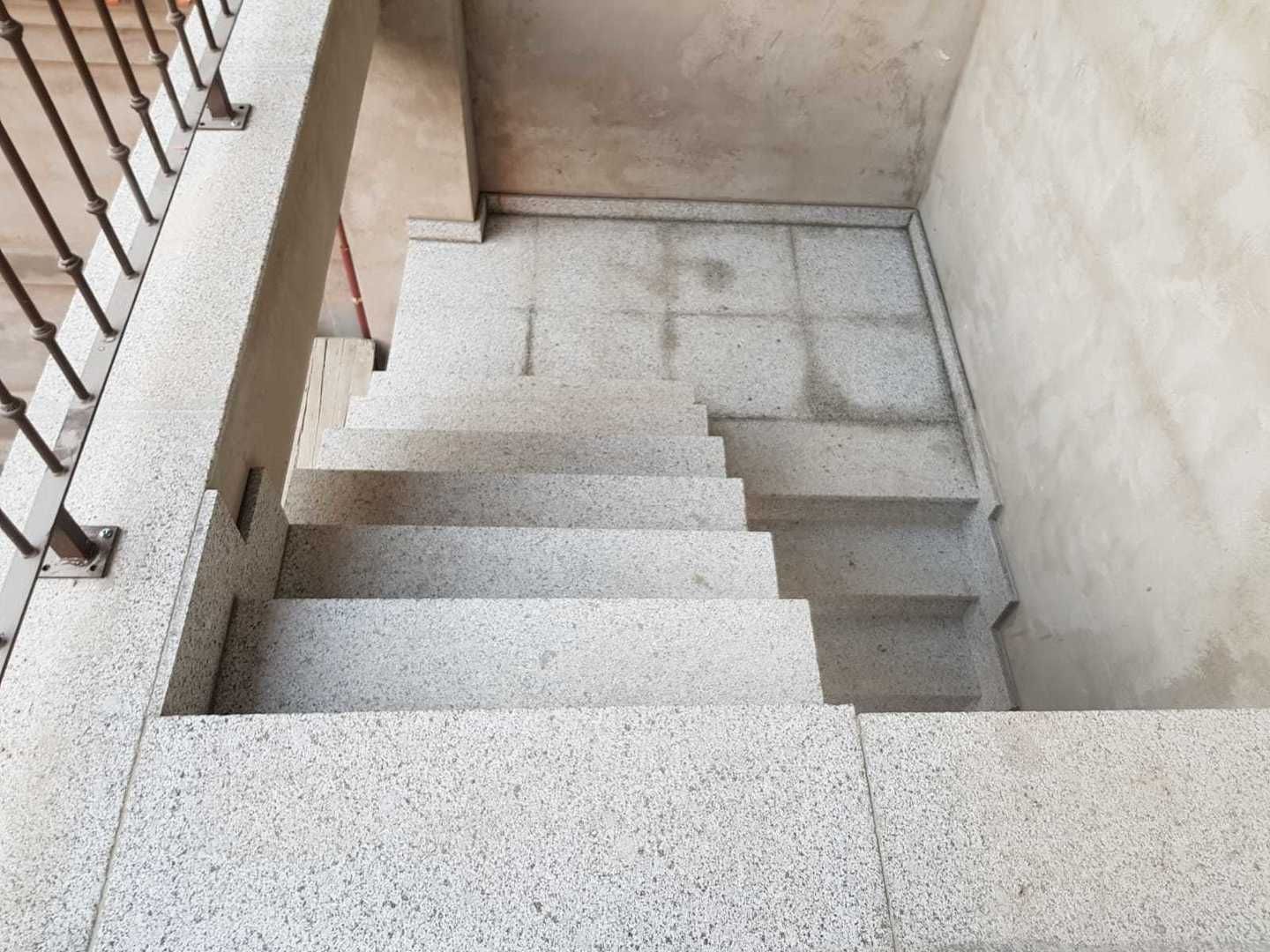 Escalera con escalones ligeramente moteados y barandilla metálica a la izquierda.