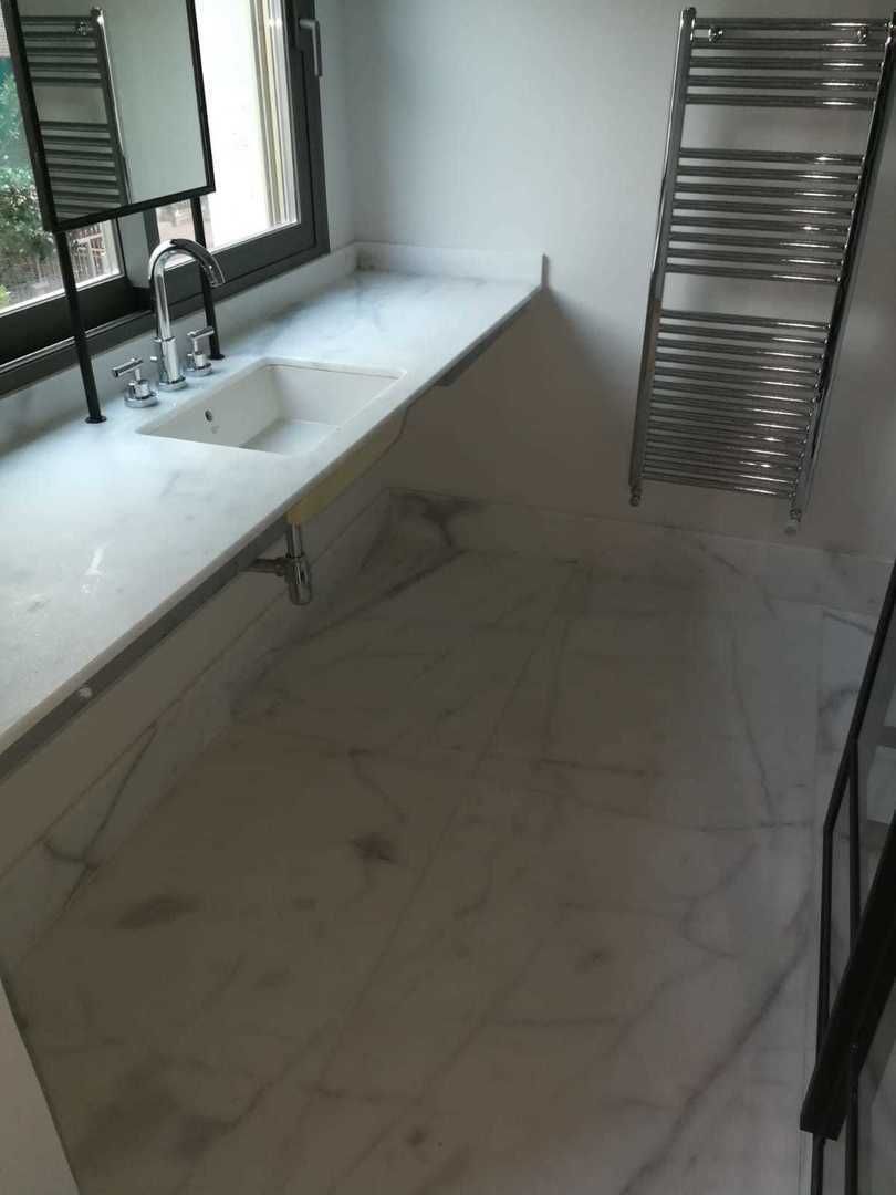 Baño con encimera y suelo de mármol blanco, toallero y lavabo.