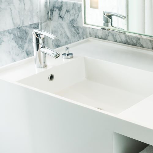 Lavabo de baño blanco con grifo cromado y dispensador de jabón, salpicadero de mármol y espejo.