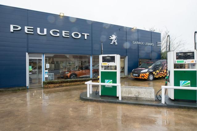 Un SUV orange dans un showroom, vitrine donnant sur des voitures à l'extérieur.