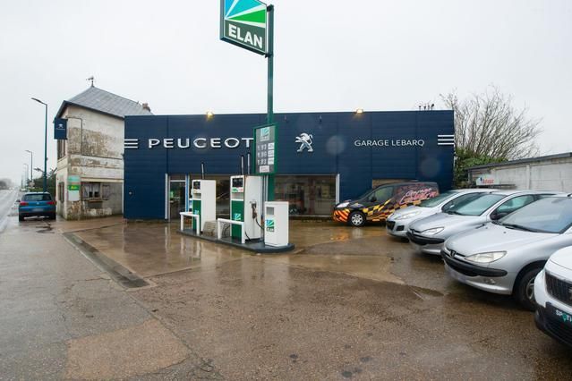 Concessionnaire Peugeot avec pompes à essence ; véhicules stationnés devant. Panneau de station-service ELAN.
