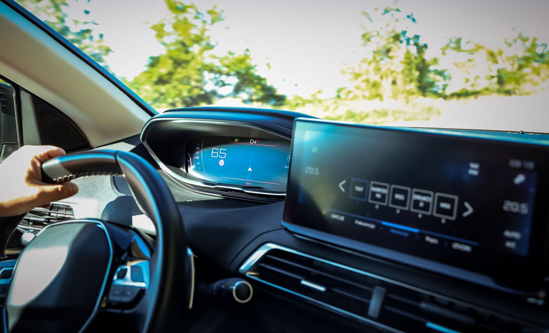 Vue intérieure de la voiture : main sur le volant, tableau de bord avec affichage numérique.