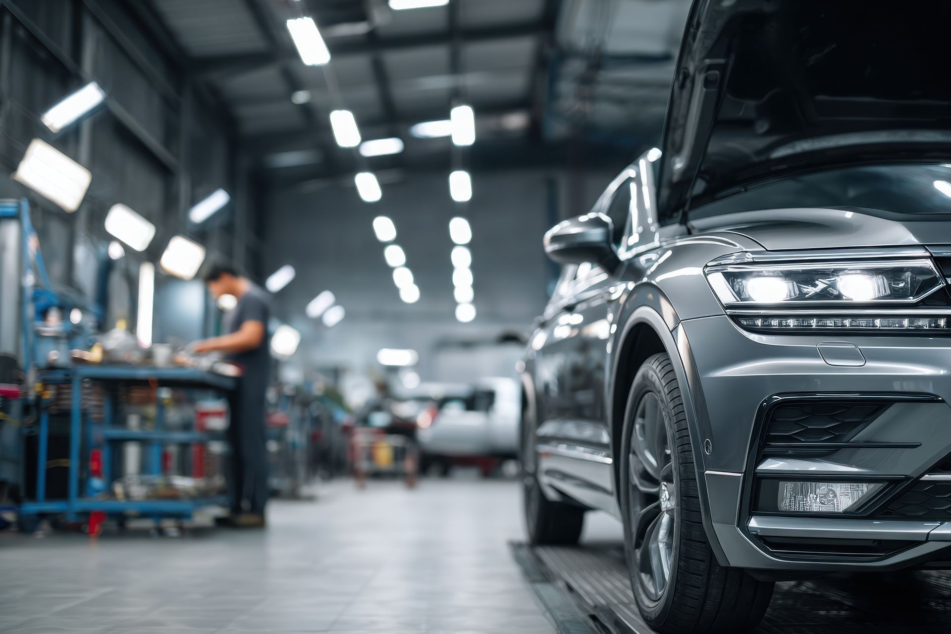 SUV sombre dans un garage, capot ouvert, un mécanicien travaillant sur une voiture en arrière-plan, éclairage fluorescent.