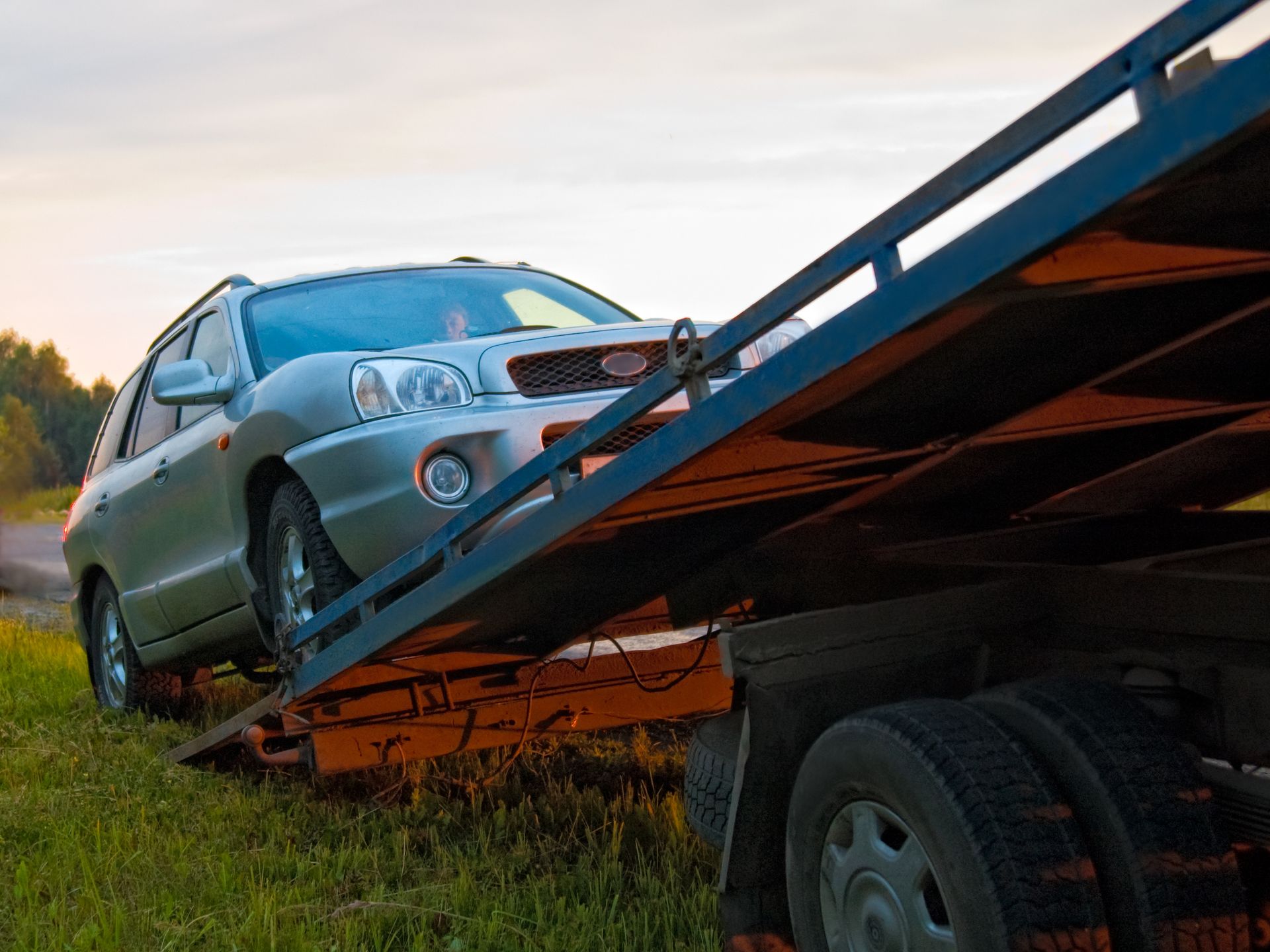 Un SUV argenté est chargé sur une dépanneuse à plateau en bordure de route herbeuse.