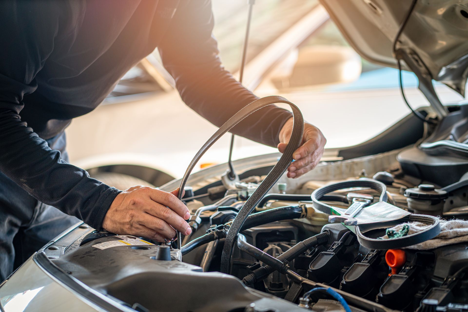 Un mécanicien inspecte le moteur d'une voiture, une courroie à la main, dans un garage.