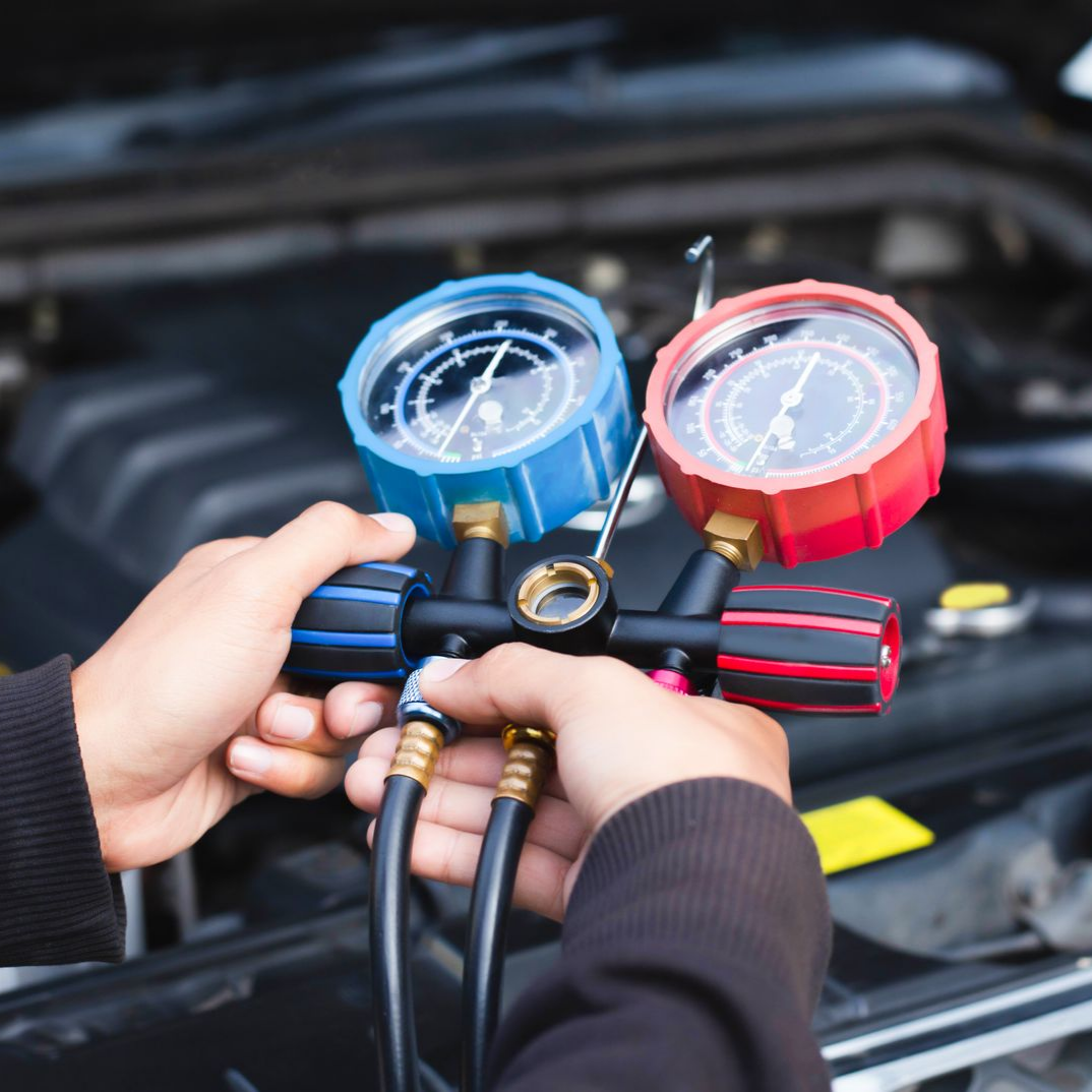 Des mains tiennent un collecteur de manomètres de climatisation avec des manomètres fixés au moteur d'une voiture.