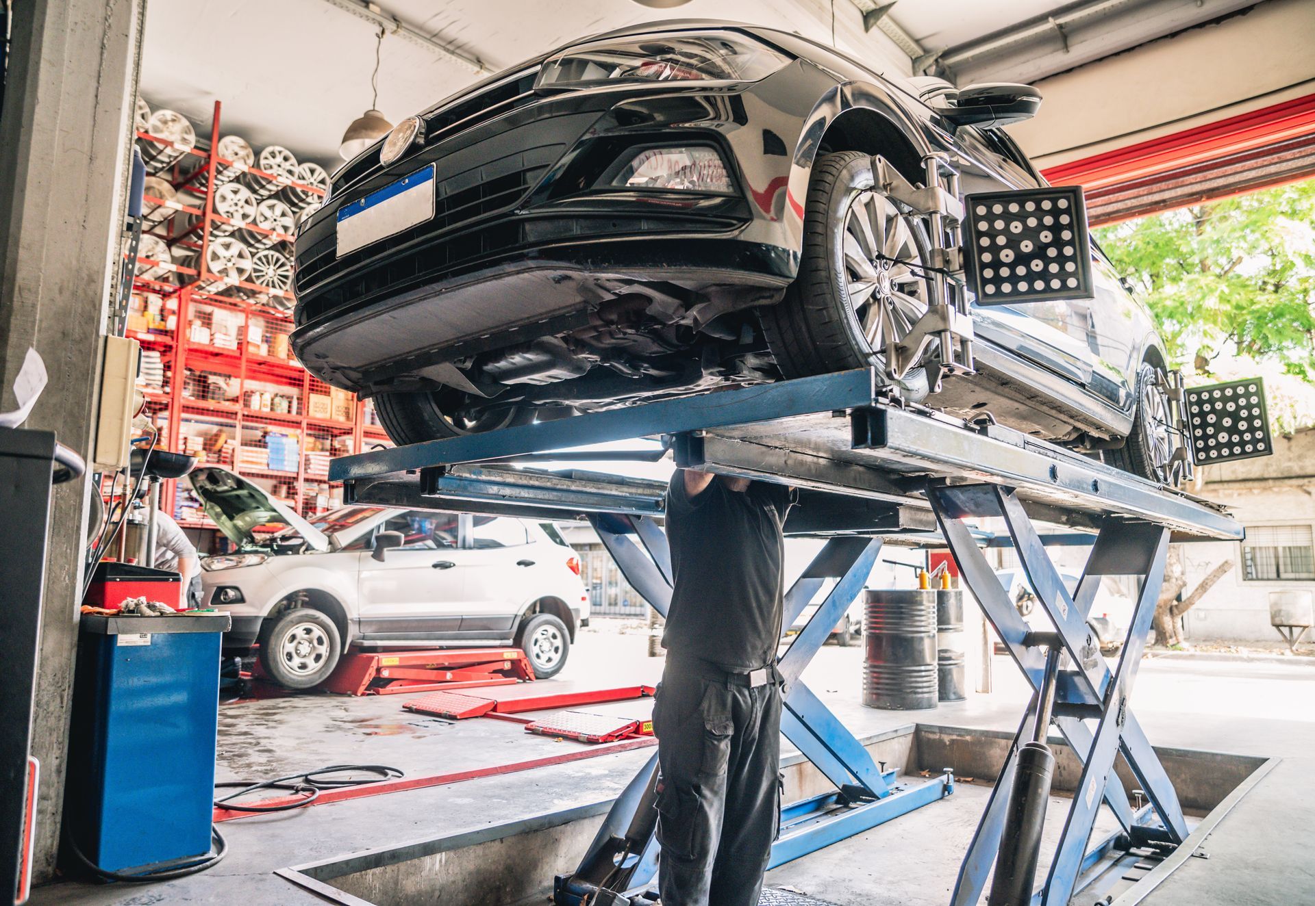 Voiture sur un pont élévateur dans un garage ; un mécanicien travaille dessous.