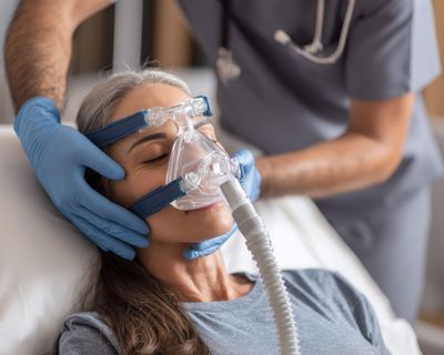 Un infirmier est en train de manipuler l'appareil respiratoire d'une femme couchée sur un lit
