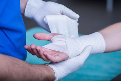 Une personne en tenue bleue enroule un bandage autour de la main blessée d'une autre personne.