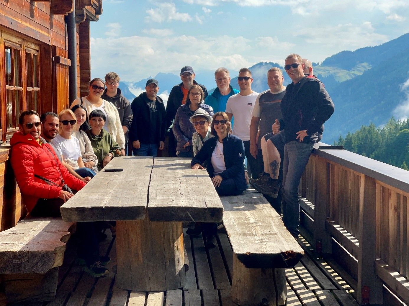A group of people standing around a wooden table on a balcony.