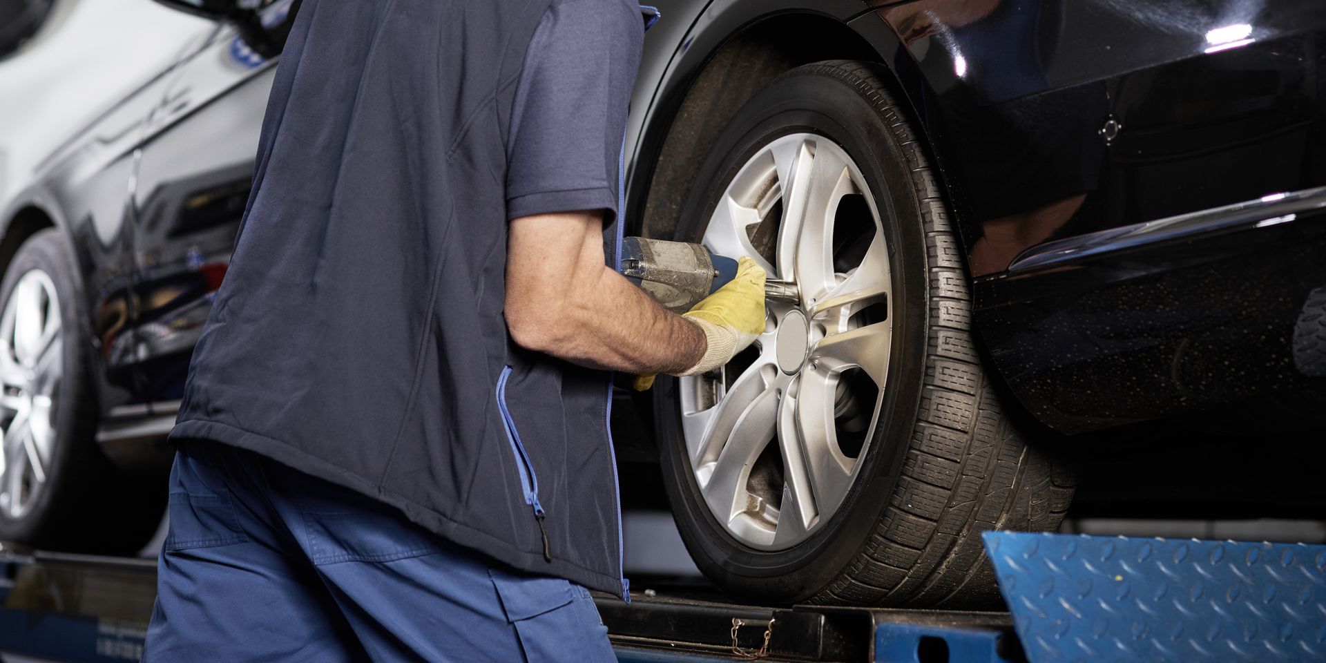 Un mécanicien travaille sur un pneu de voiture, vêtu de vêtements et de gants, dans un garage.