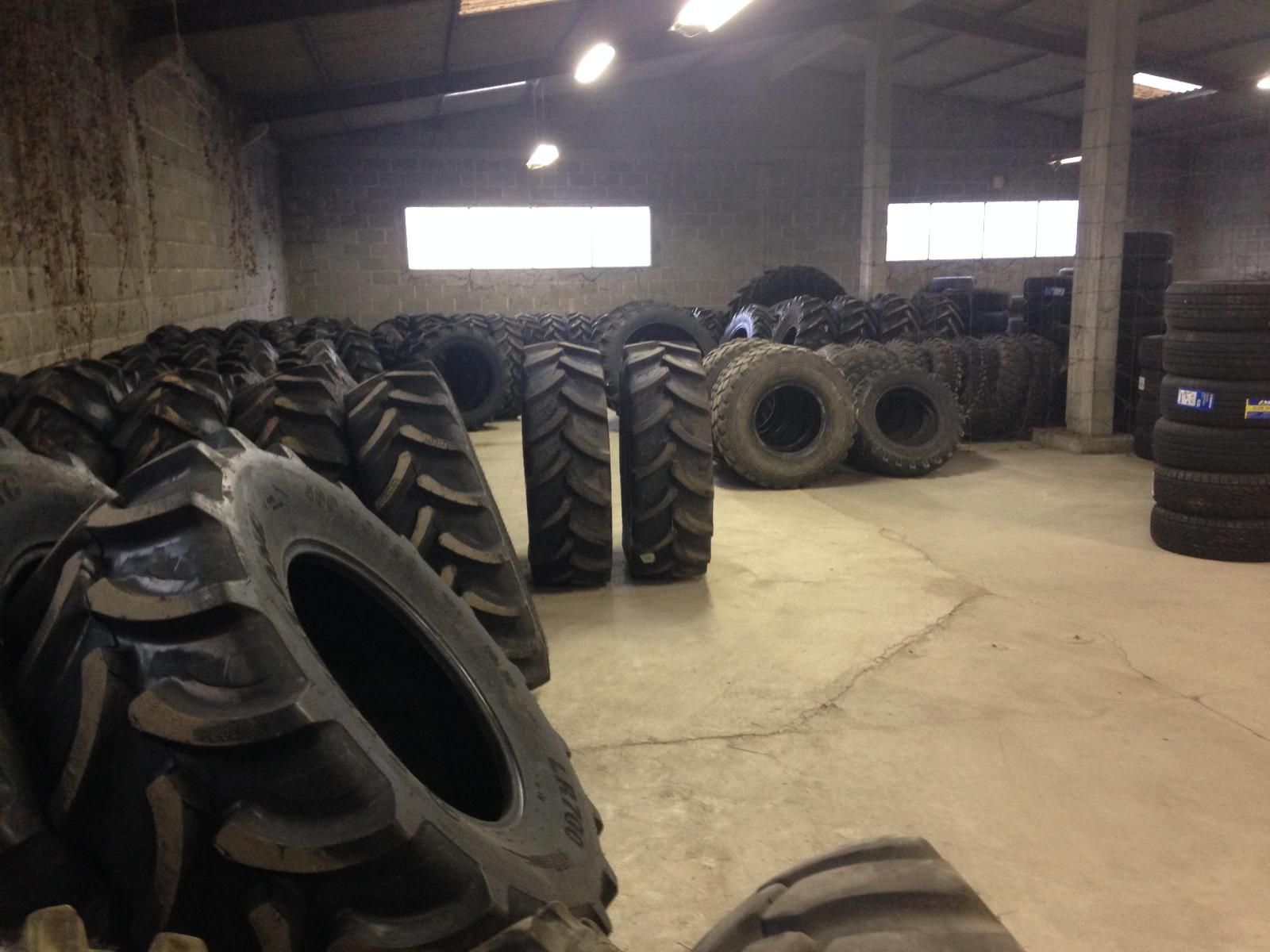 Vue intérieure d'un entrepôt rempli de piles et de rangées de gros pneus agricoles.