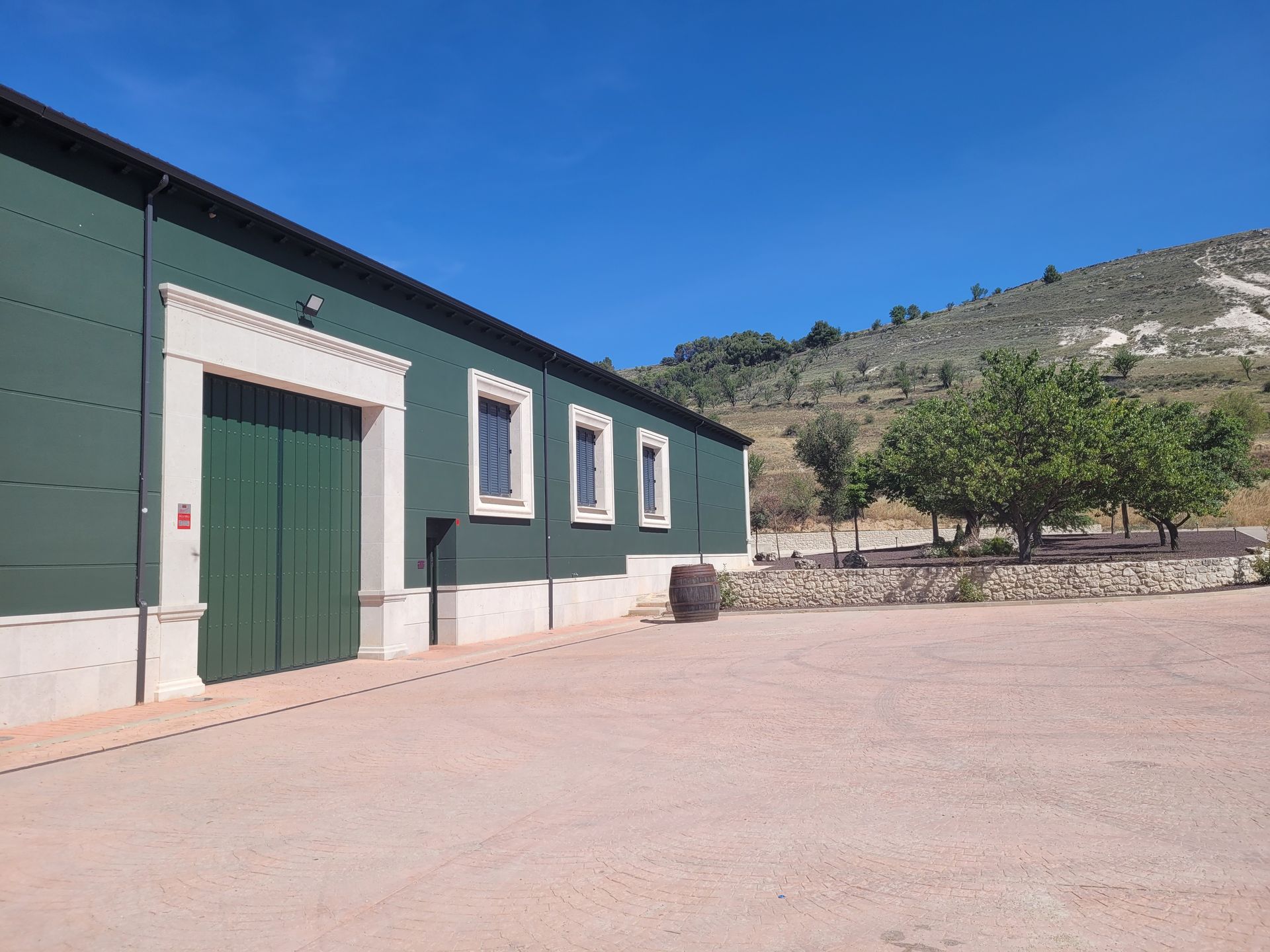 Un edificio verde con una puerta grande está ubicado encima de un campo de tierra.
