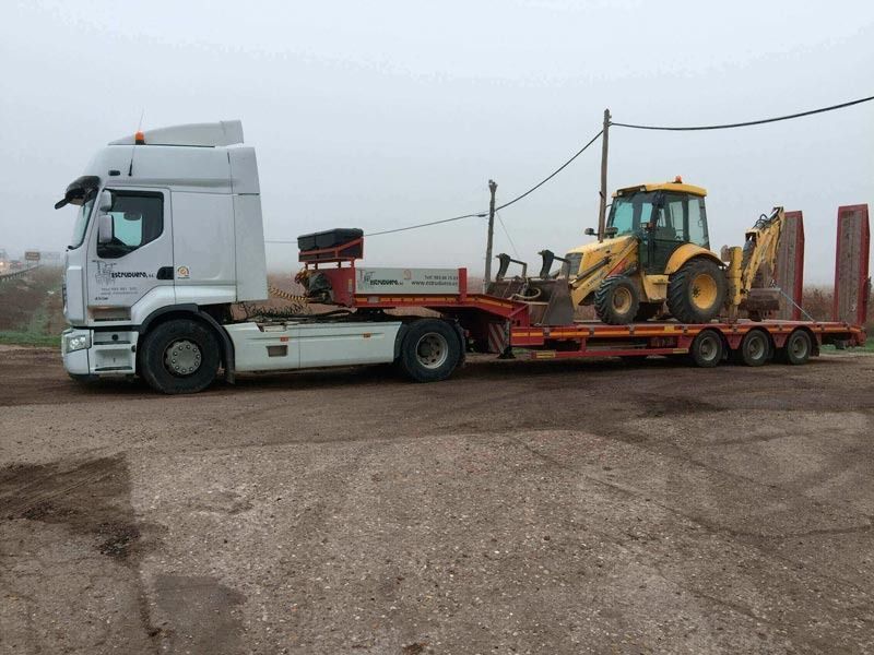 Un camión blanco transporta un tractor amarillo en un remolque.