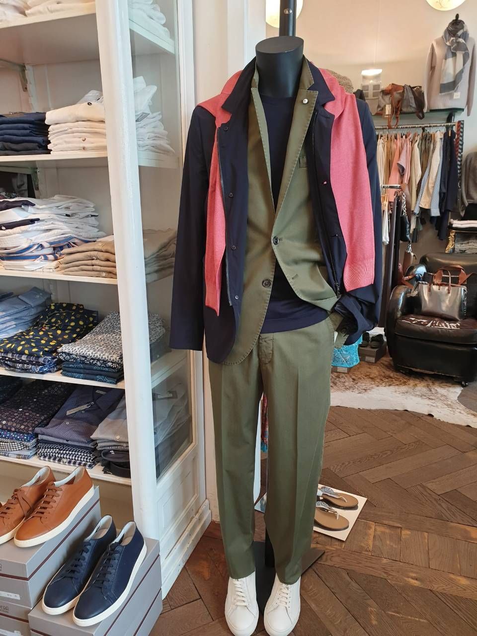 Schaufensterpuppe in einem Einzelhandelsgeschäft, die eine marineblaue und rote Jacke, einen olivgrünen Anzug und weisse Turnschuhe trägt.