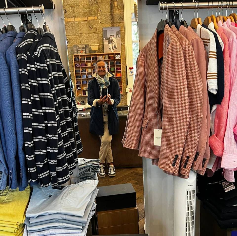 Ein Mann in einem Bekleidungsgeschäft, sein Spiegelbild. Kleiderständer mit Jacken und Hemden.