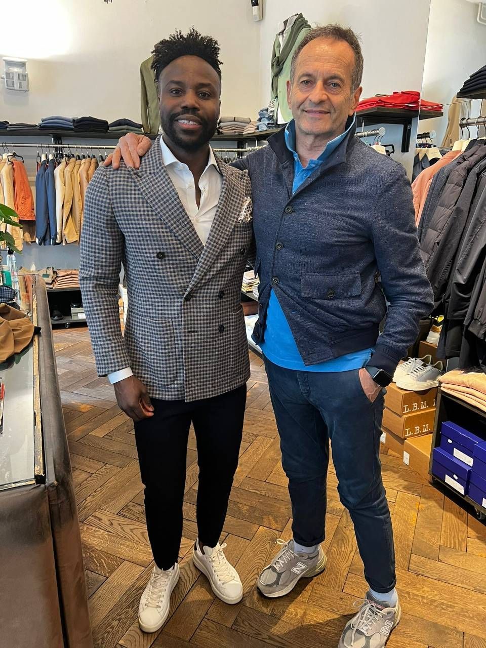 Zwei Männer in einem Bekleidungsgeschäft. Der eine trägt einen gemusterten Blazer, der andere eine blaue Jacke.
