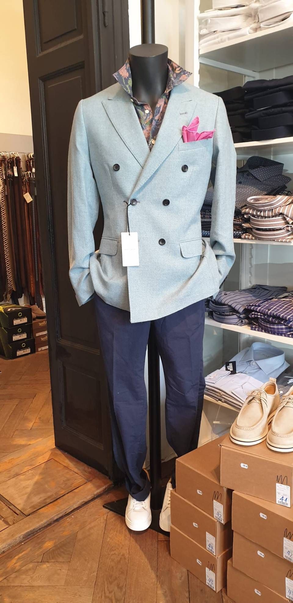 Schaufensterpuppe mit einem zweireihigen grauen Blazer, einem gemusterten Hemd, einer dunkelblauen Hose und weissen Sneakers.