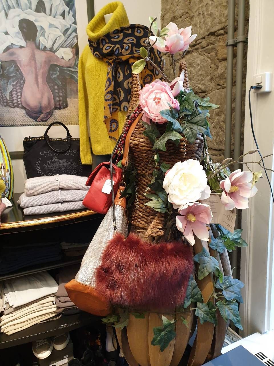 Schaufensterdekoration mit Kleidung und Handtaschen; gelber Pullover, geblümter Schal, künstliche Blumen.