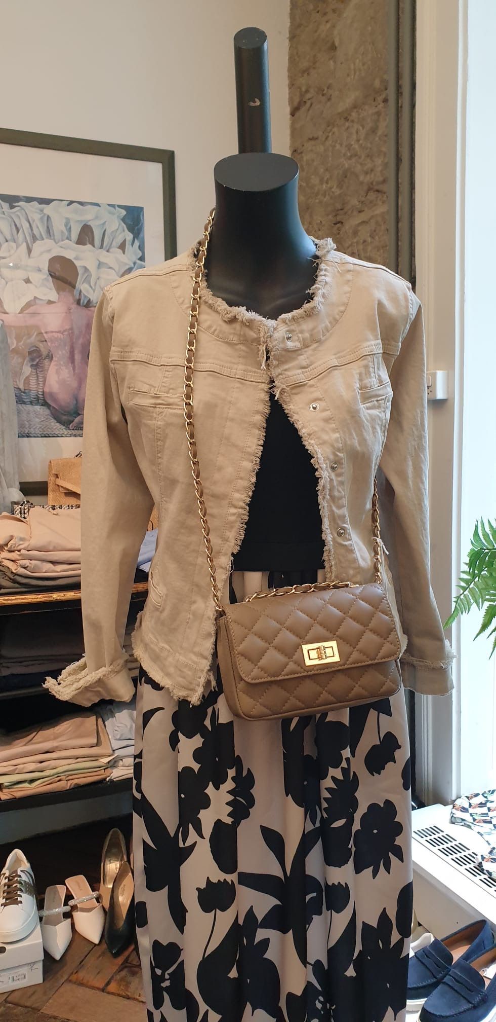 Schaufensterpuppe mit Jacke, Rock und Handtasche in einem Geschäft.