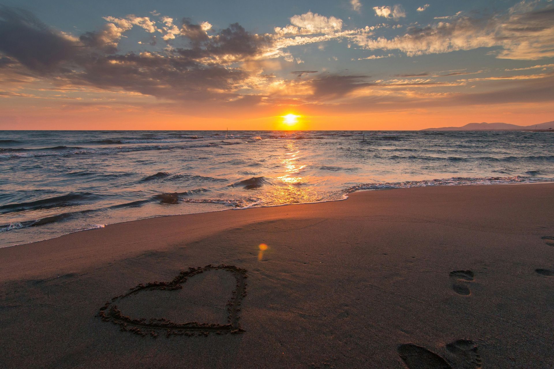 A heart is drawn in the sand on the beach at sunset.