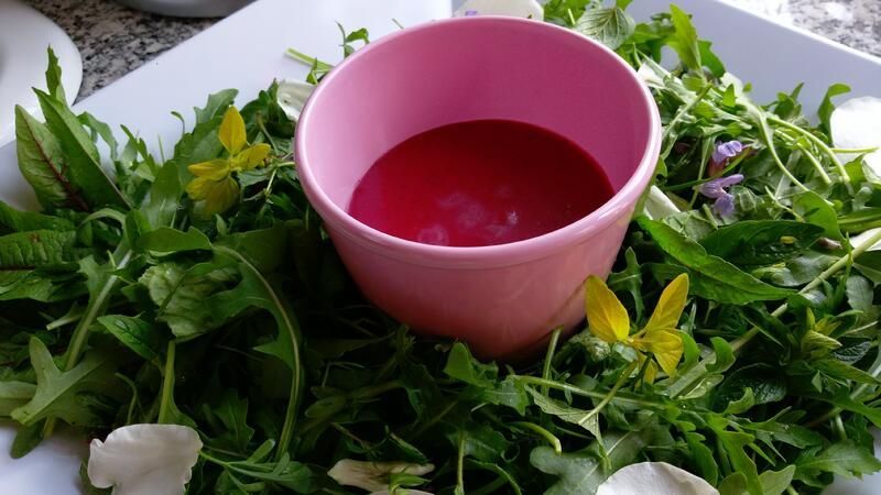 Eine Schüssel mit roter Flüssigkeit ist von grünen Blättern und Blumen umgeben.