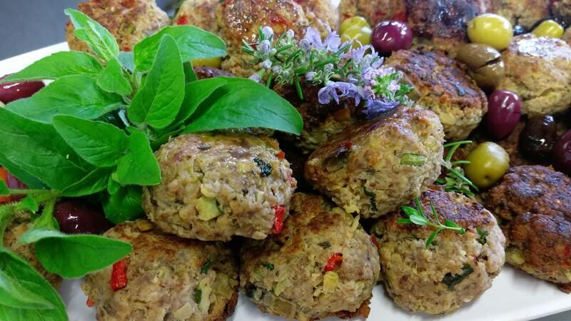 Ein weißer Teller, belegt mit Fleischbällchen, Oliven und Kräutern.