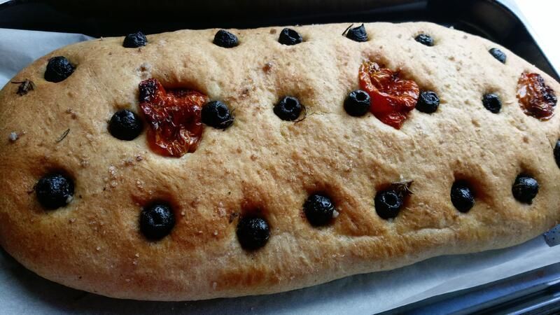 Ein Laib Brot mit Oliven und Tomaten darauf