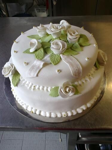 Ein weißer Kuchen mit weißen Rosen und grünen Blättern darauf