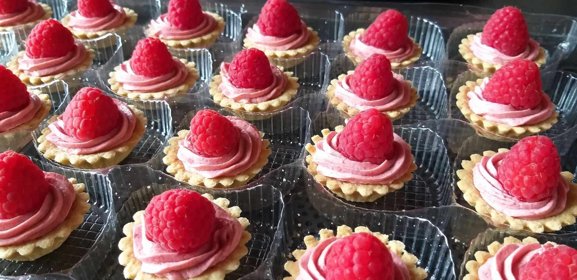 Ein Tablett mit Cupcakes, obenauf Himbeeren.