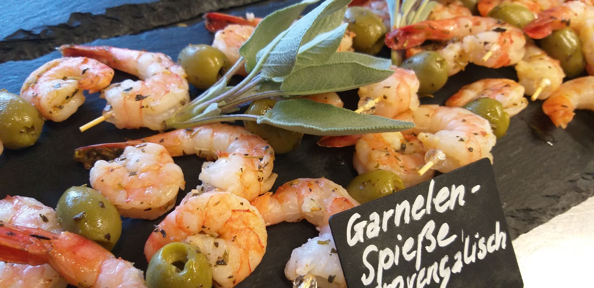 Ein Teller mit Garnelen und Oliven mit einem Schild mit der Aufschrift „Garnelen Spiesse“