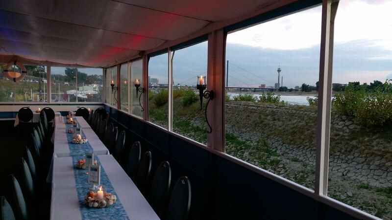 Ein langer Tisch mit Kerzen darauf steht vor einem Fenster mit Aussicht auf ein Gewässer.